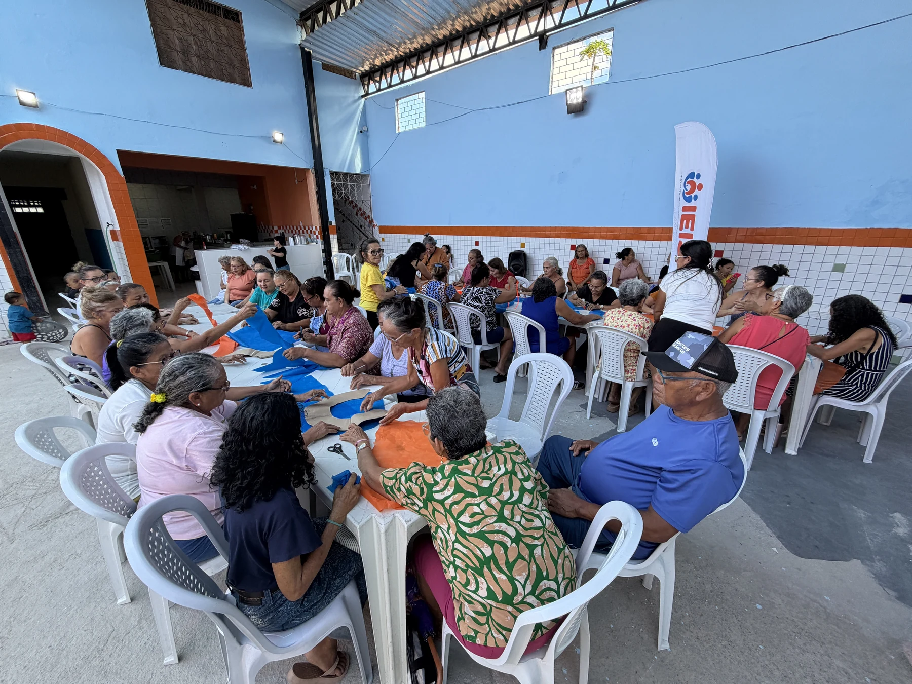 Grupo reunido em torno das mesas de trabalho para uma atividade artesanal coletiva, com troca de experiências e participação das pessoas idosas · 2026