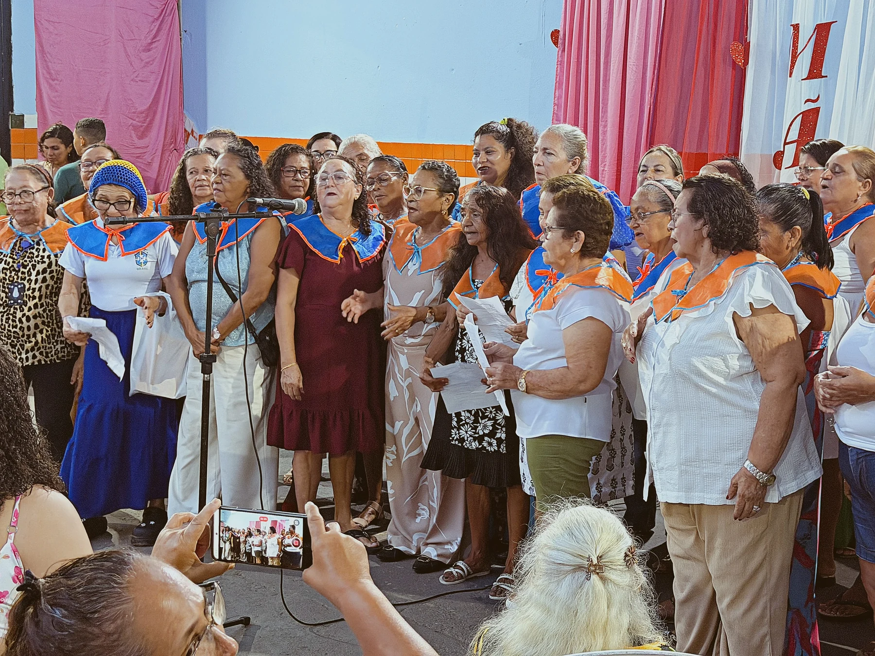 Apresentação do coral do Tempo de Viver, com uso de microfones e adereços que compõem a expressão coletiva do grupo · 2026